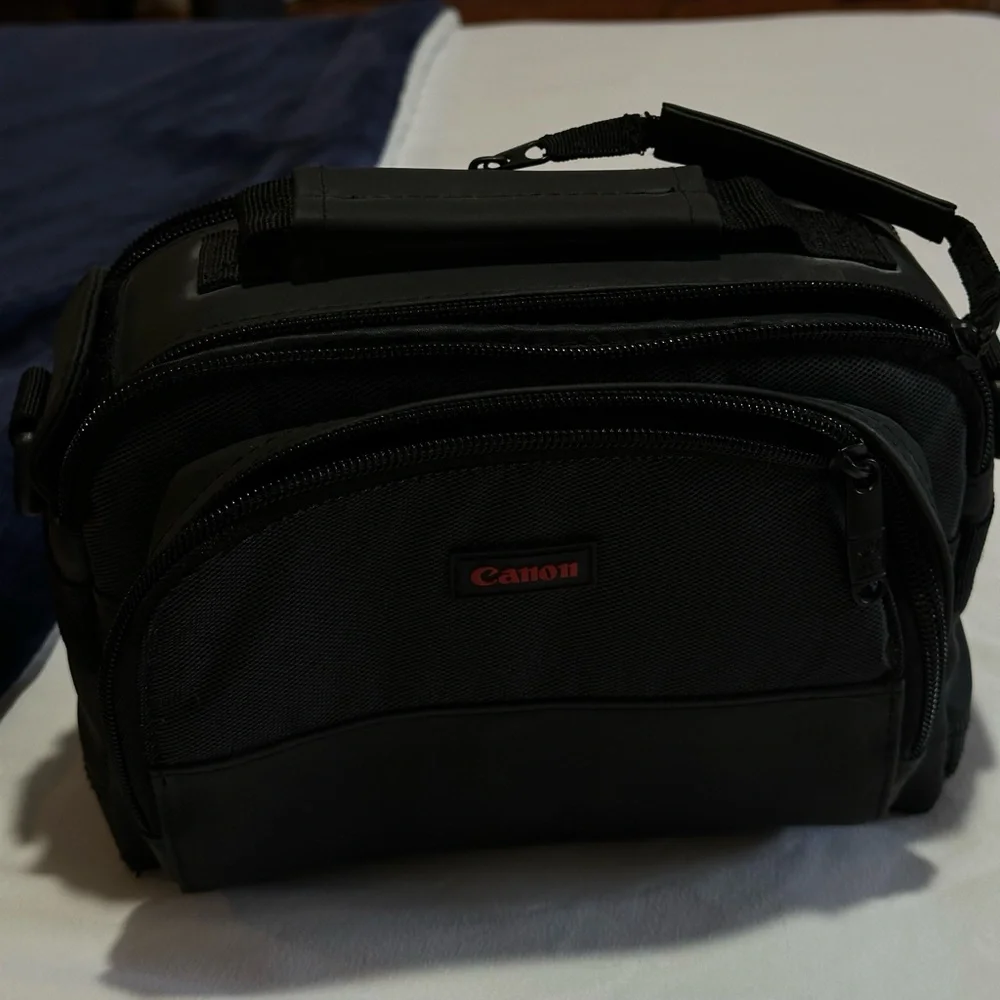 Canon black camera bag with zipper packets, and a handle at the top.